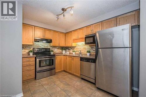 Kitchen featuring appliances with stainless steel finishes, a textured ceiling, under cabinet range hood, tasteful backsplash, and light stone countertops - 27 Max Becker Drive, Kitchener, ON - Indoor Photo Showing Kitchen