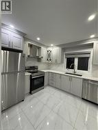 Kitchen with fridge, stainless steel stove, light marble finish floors, gray cabinets, and exhaust hood - 