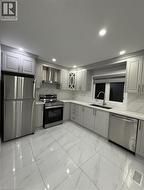 Kitchen featuring stainless steel appliances, gray cabinetry, light marble finish floors, wall chimney range hood, and backsplash - 
