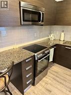 Kitchen with modern cabinets, stainless steel appliances, light stone countertops, backsplash, and light vinyl flooring - 