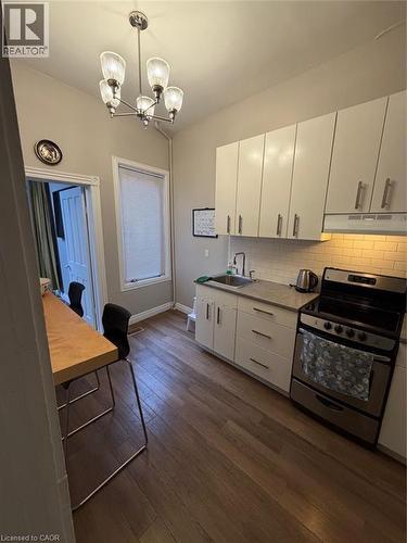 Kitchen with stove, dark wood-style flooring, a chandelier, white cabinetry, and pendant lighting - 175 John Street S, Hamilton, ON 