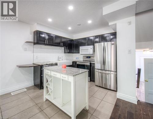 Kitchen with appliances with stainless steel finishes, light stone counters, tasteful backsplash, open shelves, and a center island - 20 Bankside Drive, Kitchener, ON - Indoor Photo Showing Kitchen