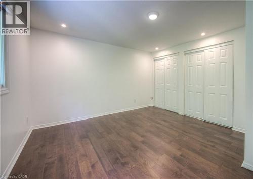Unfurnished bedroom featuring two closets, dark wood-style floors, and recessed lighting - 20 Bankside Drive, Kitchener, ON - Indoor Photo Showing Other Room