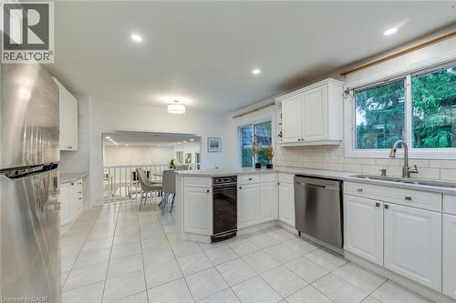 Kitchen with appliances with stainless steel finishes, white cabinetry, light tile patterned floors, a peninsula, and decorative backsplash - 170 Cavendish Court, Oakville, ON - Indoor Photo Showing Kitchen With Double Sink