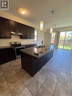 Kitchen with an island with sink, stove, a kitchen breakfast bar, decorative light fixtures, and dark stone countertops - 