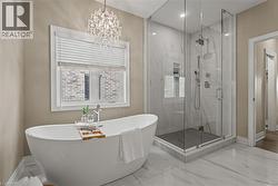 Bathroom featuring a freestanding tub, a marble finish shower, marble tiled flooring, and a chandelier - 