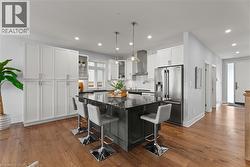 Kitchen featuring a breakfast bar area, high quality fridge, hanging light fixtures, dark stone countertops, and white cabinetry - 
