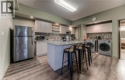 Kitchen with washer and clothes dryer, a kitchen island with sink, hardwood / wood-style flooring, a kitchen bar, and stainless steel appliances - 8 Hickory Street W Unit# 401, Waterloo, ON - Indoor