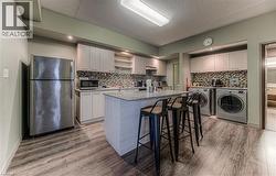 Kitchen with washer and clothes dryer, a kitchen island with sink, hardwood / wood-style flooring, a kitchen bar, and stainless steel appliances - 