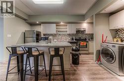 Kitchen featuring a kitchen breakfast bar, washer / dryer, light stone counters, and appliances with stainless steel finishes - 