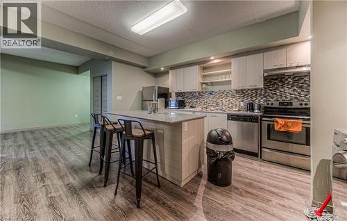 Kitchen featuring light stone countertops, backsplash, a breakfast bar, stainless steel appliances, and light hardwood / wood-style flooring - 8 Hickory Street W Unit# 401, Waterloo, ON - Indoor Photo Showing Kitchen