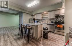 Kitchen featuring light stone countertops, backsplash, a breakfast bar, stainless steel appliances, and light hardwood / wood-style flooring - 