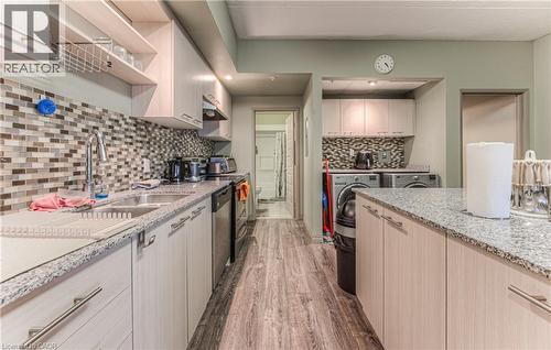 Kitchen with backsplash, sink, stainless steel dishwasher, washing machine and dryer, and light brown cabinetry - 8 Hickory Street W Unit# 401, Waterloo, ON - Indoor Photo Showing Kitchen With Double Sink