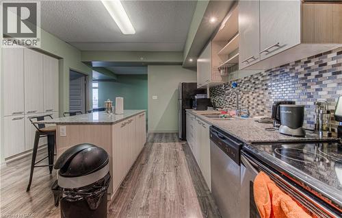Kitchen with backsplash, light stone counters, a breakfast bar, a textured ceiling, and stainless steel appliances - 8 Hickory Street W Unit# 401, Waterloo, ON - Indoor Photo Showing Kitchen