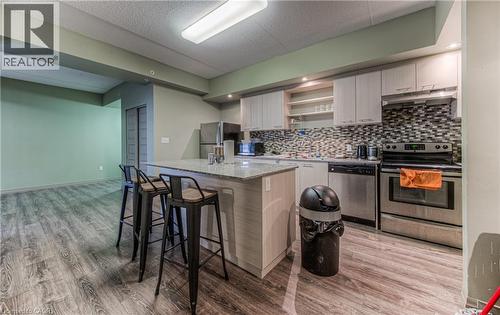 Kitchen featuring backsplash, hardwood / wood-style flooring, light stone counters, appliances with stainless steel finishes, and a kitchen bar - 8 Hickory Street W Unit# 401, Waterloo, ON - Indoor Photo Showing Kitchen With Upgraded Kitchen