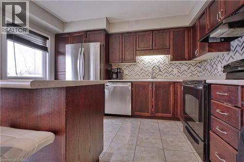 Kitchen with stainless steel appliances, under cabinet range hood, light tile patterned floors, light countertops, and reddish brown cabinets - 206 Westmeadow Drive, Kitchener, ON - Indoor Photo Showing Kitchen With Stainless Steel Kitchen