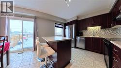 Kitchen featuring a kitchen island, light tile patterned flooring, a breakfast bar area, and stainless steel appliances - 