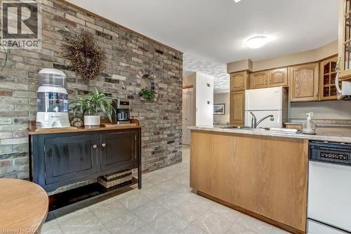 Kitchen featuring glass insert cabinets, white appliances, a peninsula, light flooring, and brown cabinets - 2 Falls Crescent, Simcoe, ON - Indoor Photo Showing Kitchen With Double Sink