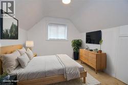 Bedroom staged featuring light colored carpet, vaulted ceiling, and a textured ceiling - 