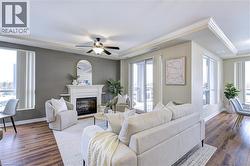 Living room featuring a glass covered fireplace, ceiling fan, dark wood-style flooring, ornamental molding, and a raised ceiling - 