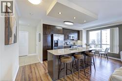 Kitchen with dark brown cabinets, a kitchen bar, stainless steel appliances, light stone counters, and light wood-style floors - 