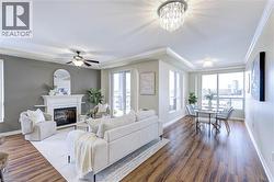 Living room with a raised ceiling, ornamental molding, a chandelier, a glass covered fireplace, and dark wood-type flooring - 