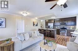 Living room with a ceiling fan, light wood-type flooring, crown molding, and a chandelier - 