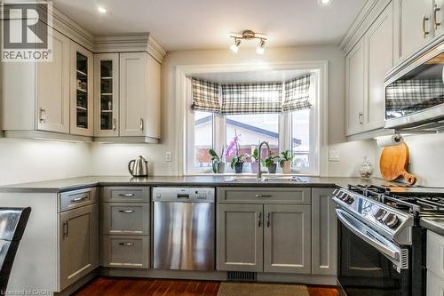 Kitchen with gray cabinetry, stainless steel appliances, dark wood finished floors, glass insert cabinets, and dark countertops - 22 Redwing Road, Hamilton, ON - Indoor Photo Showing Kitchen With Double Sink With Upgraded Kitchen