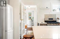 Kitchen featuring freestanding refrigerator, stainless steel gas range, tasteful backsplash, light wood-style floors, and light stone counters - 