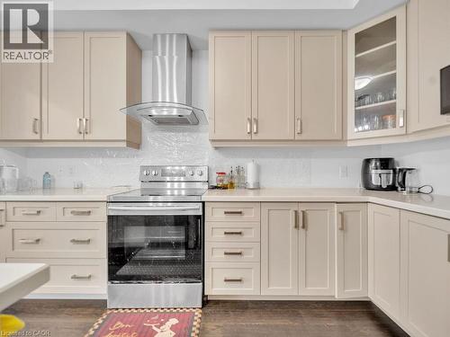 Kitchen with stainless steel electric stove, cream cabinetry, ventilation hood, glass insert cabinets, and light stone counters - 30 Times Square Boulevard, Hamilton, ON - Indoor Photo Showing Kitchen