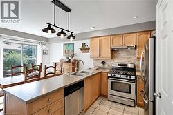 Kitchen with stainless steel appliances, decorative backsplash, a peninsula, light tile patterned floors, and hanging light fixtures - 
