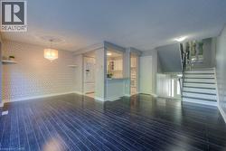 Unfurnished living room featuring wallpapered walls, stairs, dark wood-type flooring, and a textured ceiling - 