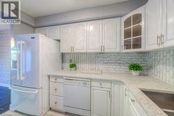 Kitchen with glass insert cabinets, white cabinetry, white appliances, and light stone counters - 