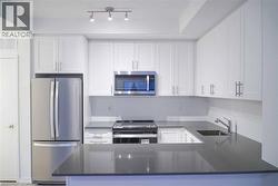 Kitchen with stainless steel appliances, white cabinetry, dark stone counters, and a peninsula - 