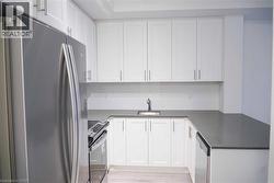 Kitchen featuring stainless steel appliances, white cabinets, light wood-style floors, dark stone counters, and a peninsula - 