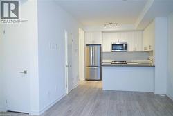 Kitchen with stainless steel appliances, white cabinetry, light wood finished floors, dark countertops, and a peninsula - 