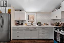 Kitchen featuring appliances with stainless steel finishes, white cabinetry, tasteful backsplash, dark wood finished floors, and light stone countertops - 