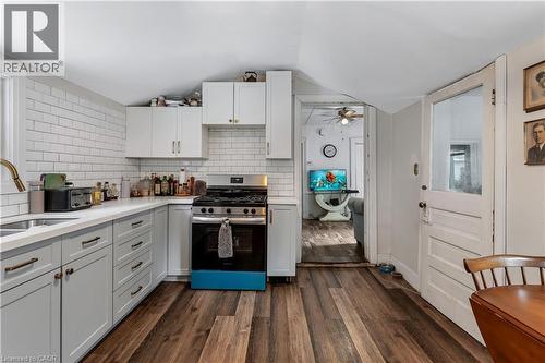 Kitchen with stainless steel gas range, decorative backsplash, dark wood-style floors, white cabinets, and lofted ceiling - 193 Locke Street N, Hamilton, ON - Indoor Photo Showing Kitchen With Double Sink