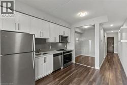 Kitchen with appliances with stainless steel finishes, white cabinets, decorative backsplash, and dark wood-style flooring - 