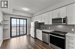 Kitchen featuring appliances with stainless steel finishes, white cabinets, dark wood-style floors, decorative backsplash, and light stone counters - 