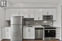 Kitchen featuring white cabinetry, stainless steel appliances, decorative backsplash, and dark wood-type flooring - 