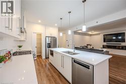 Kitchen featuring open floor plan, white cabinets, appliances with stainless steel finishes, a center island with sink, and hanging light fixtures - 
