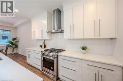 Kitchen with stainless steel range with gas stovetop, wall chimney range hood, light wood-style floors, and white cabinetry - 