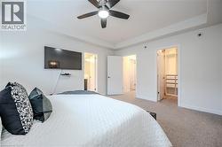 Bedroom with a walk in closet, light colored carpet, a tray ceiling, and a ceiling fan - 