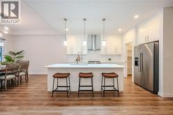 Kitchen featuring high quality fridge, white cabinets, an island with sink, pendant lighting, and a breakfast bar - 