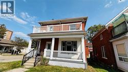 View of front of home with brick siding, covered porch, a balcony, and a front lawn - 