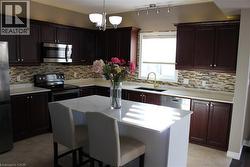 Kitchen with a kitchen breakfast bar, appliances with stainless steel finishes, decorative backsplash, light tile patterned floors, and dark brown cabinetry - 