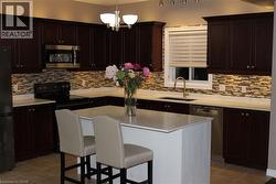 Kitchen featuring light tile patterned flooring, black appliances, decorative backsplash, and a breakfast bar - 