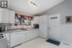 Kitchen with vaulted ceiling, white dishwasher, white cabinetry, light countertops, and light floors - 