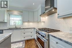 Kitchen featuring wall chimney range hood, tasteful backsplash, a sink, and stainless steel stove - 